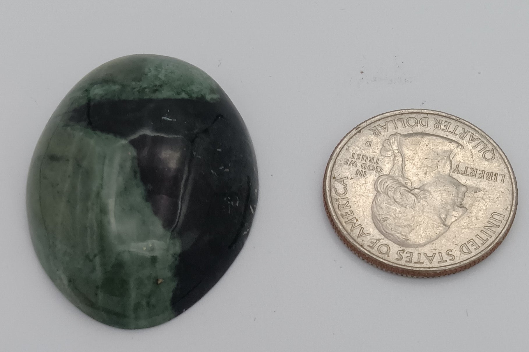 Green and black marbled stone next to a coin on a gray background