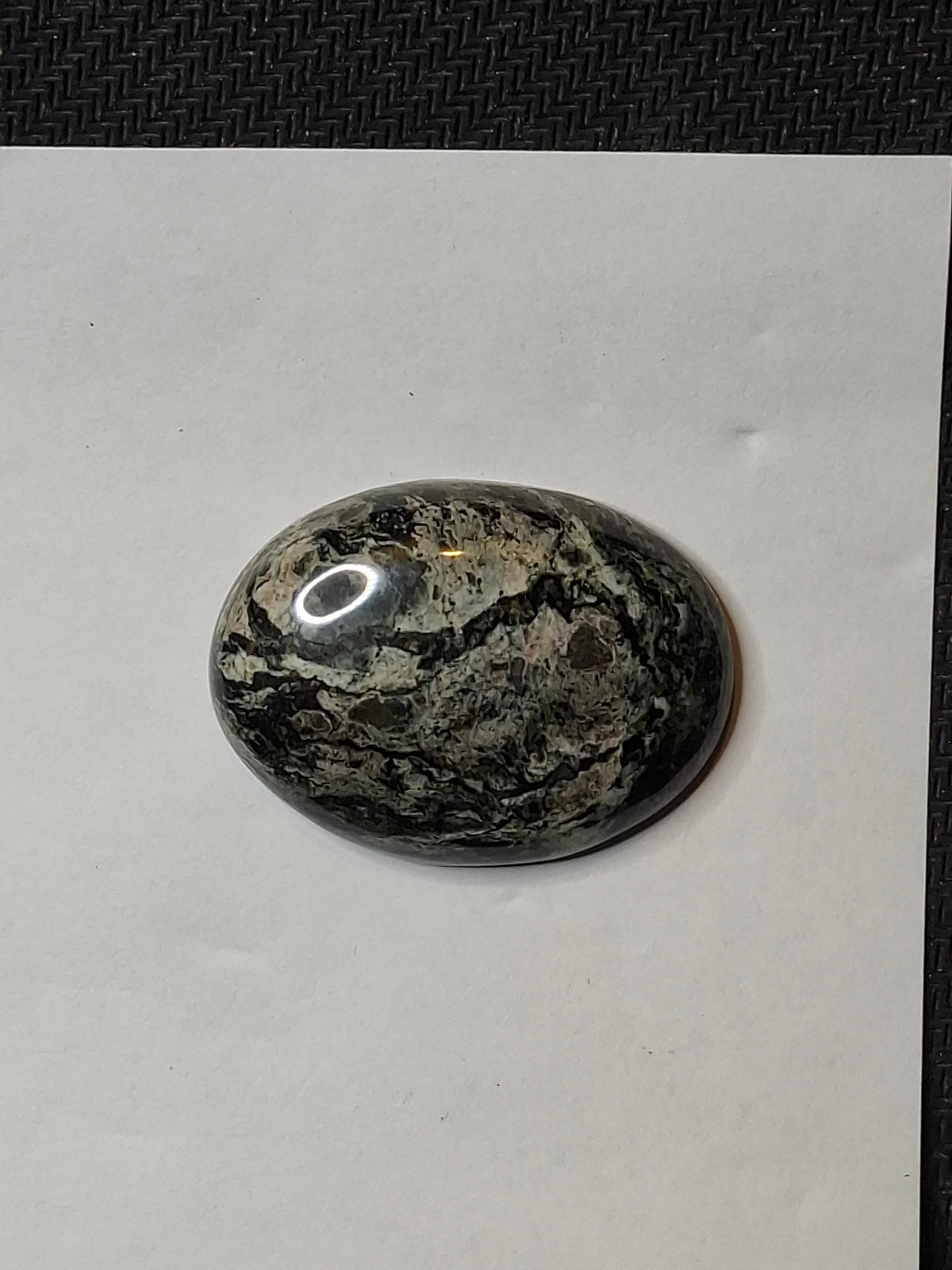 Close-up of a high-polish black and grey veined jasper cabochon, showing intricate patterns.