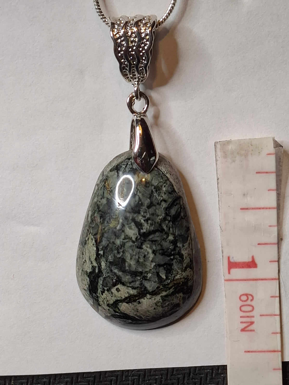 Close-up of a handcrafted Breccia Aventurine pendant with a silver-plated bail and snake chain, next to a measuring tape on a white background.