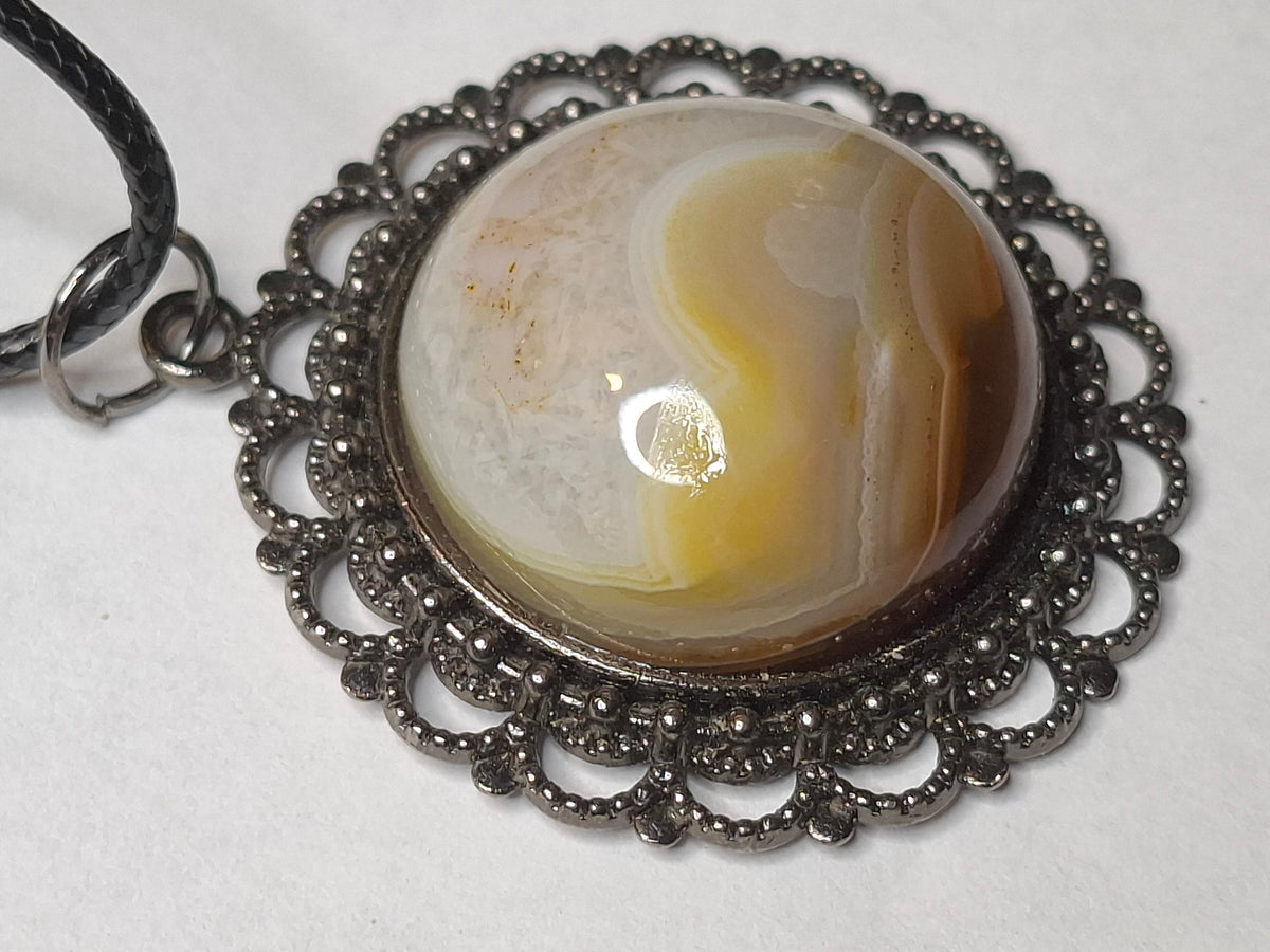 Detailed close-up of the handcrafted Botswana Agate stone, highlighting its smooth, high-polish surface and distinct caramel and white banding within an ornate dark metal bezel.
