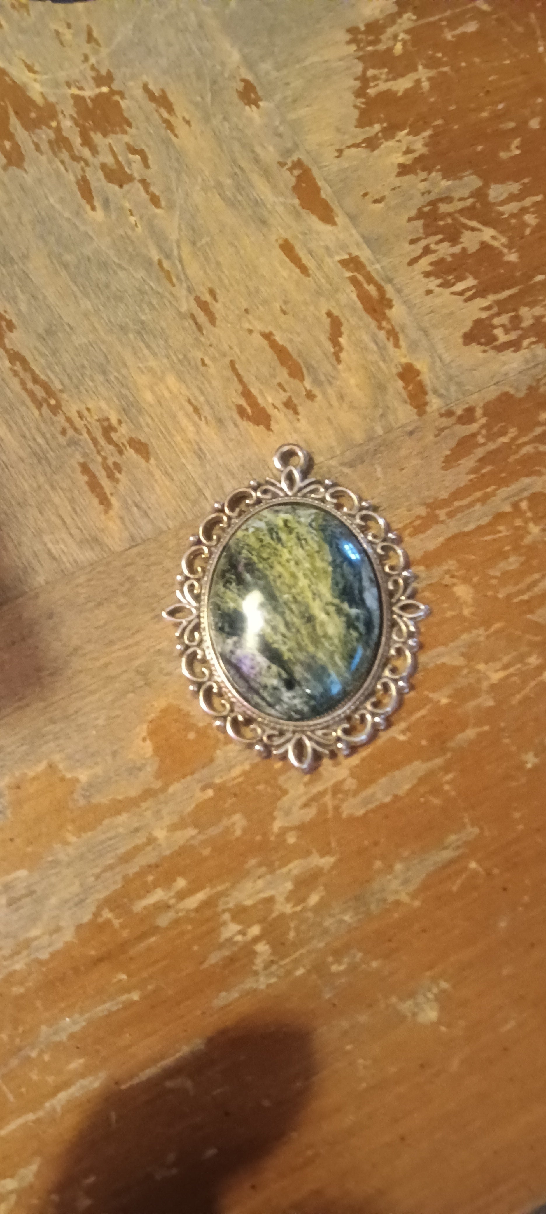 Oval stone with yellow-green, dark green, gray, and black zones, high polish, set in ornate silver filigree. Rockhound Studio.