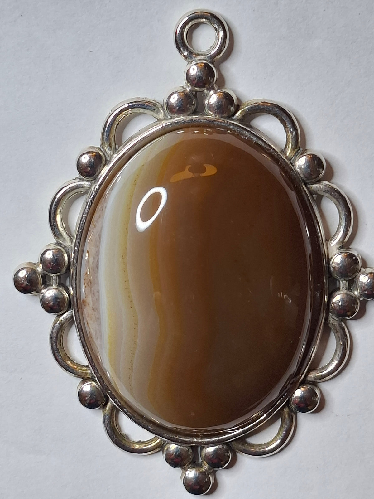 Vertical close-up of the oval Botswana Agate pendant, showing the high polish and the intricate silver-toned setting details.