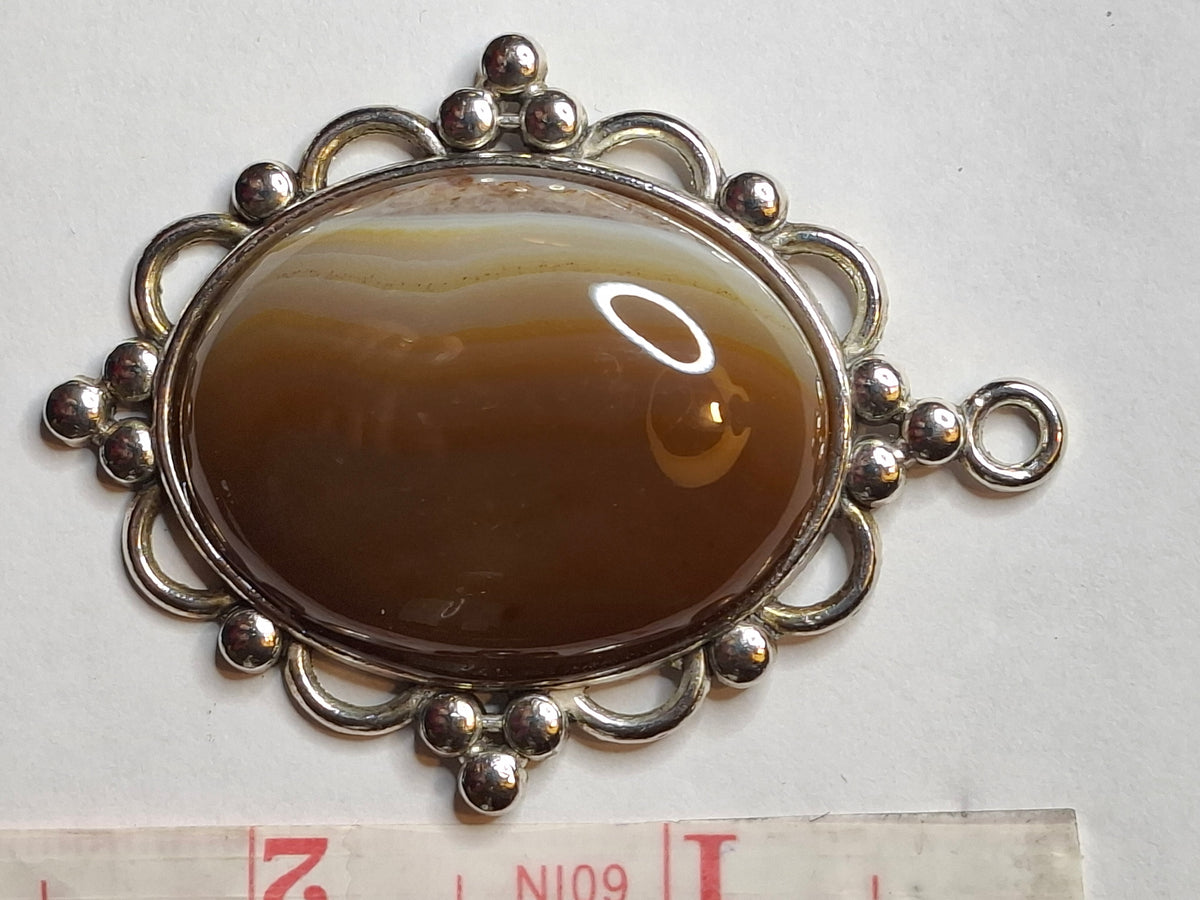 Horizontal view of the oval Botswana Agate pendant, highlighting the banded caramel and white patterns and the ornate silver-toned setting.