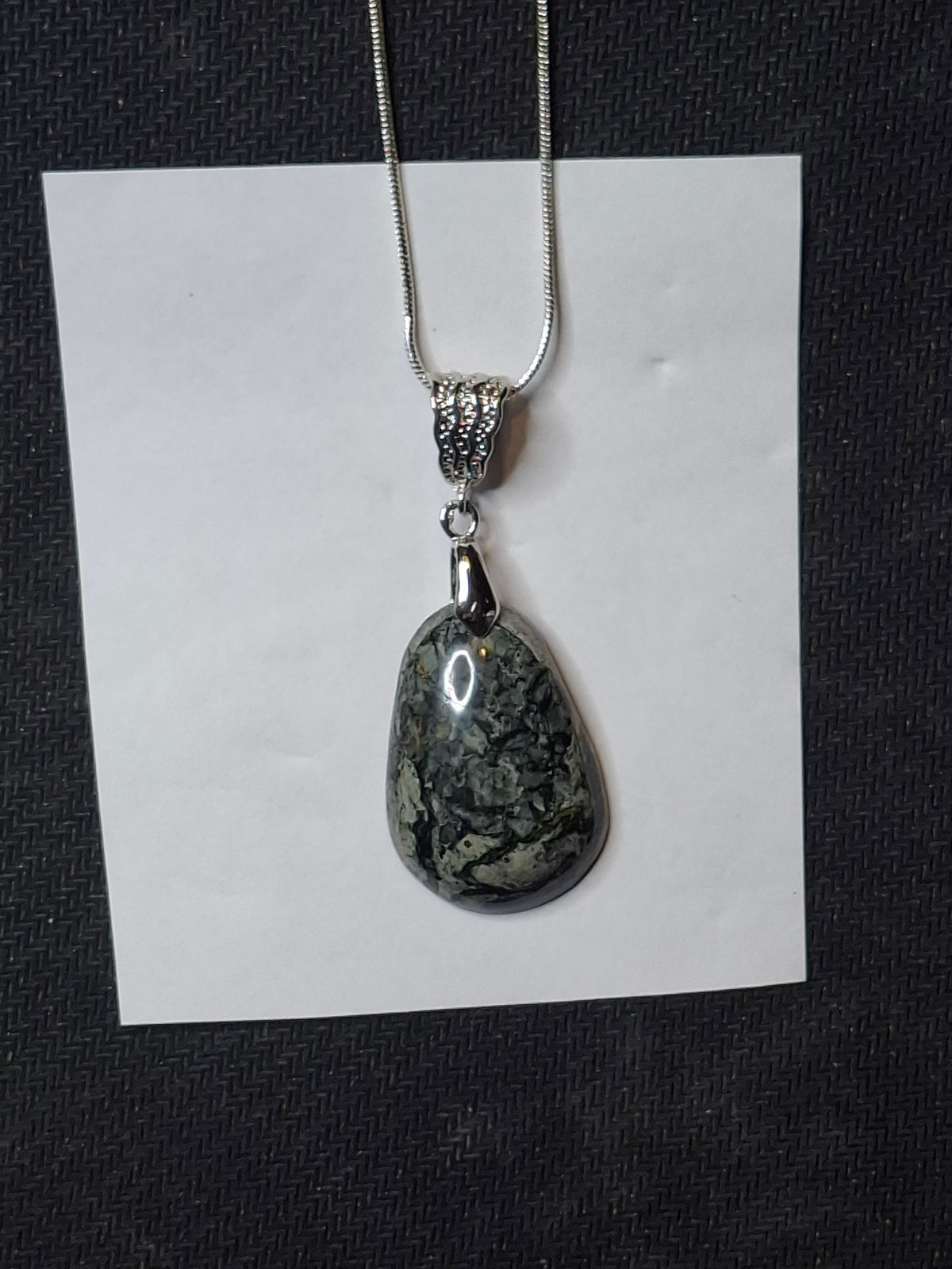 Full view of a handcrafted Breccia Aventurine pendant on a silver-plated snake chain, displayed on a small white card against a dark textured surface.